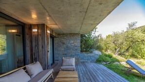 Una terraza de madera con un muro de piedra, un banco acolchado y una silla de descanso.
