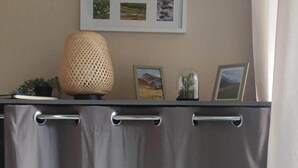 A room with a curtain-covered partition, a wall-mounted picture frame with multiple photos, and a textured lamp on a table. - Renovated 4-person studio with lake view Artouste Fabrège (Laruns)