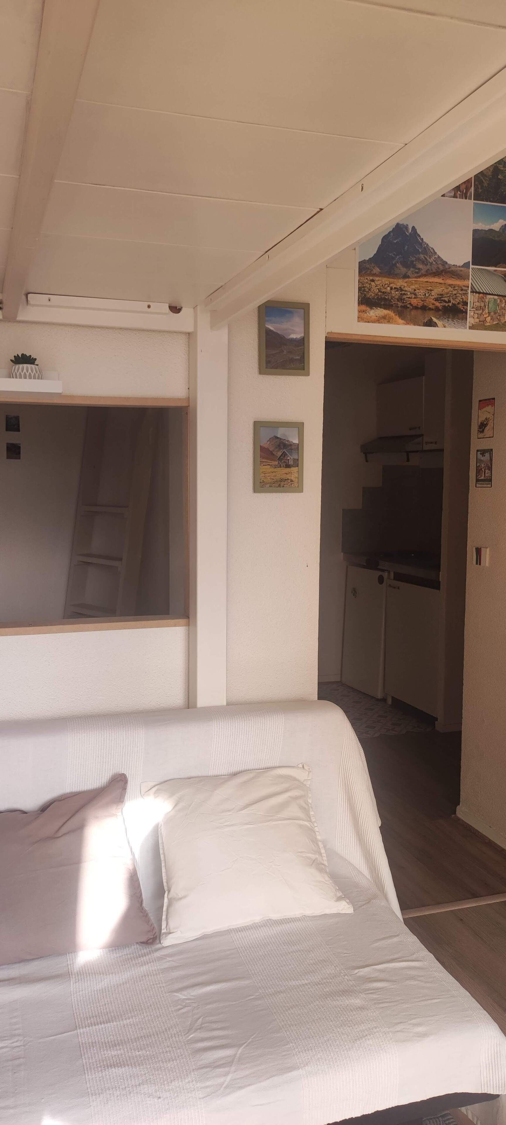 A bedroom with a bed, a window, a kitchenette, and a staircase.