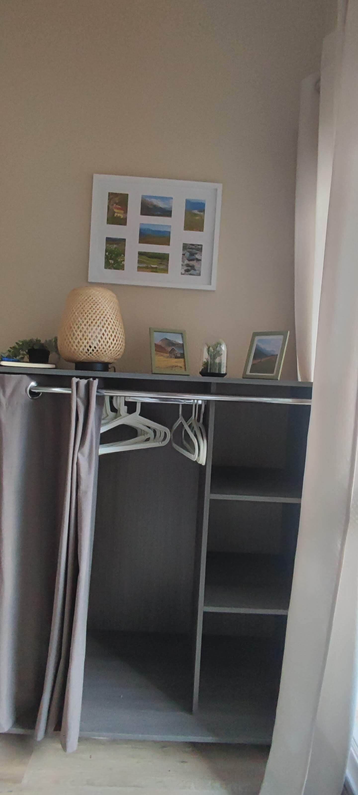 Een kamer met een metalen bureau, een hangmand, een lijst met een afbeelding en een gordijn.