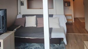 A bunk bed with a desk and a television, a small kitchen area, and a living space with a couch and a wall of pictures. - Renovated 4-person studio with lake view Artouste Fabrège (Laruns)