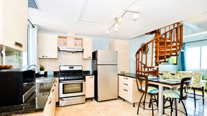 A modern kitchen with stainless steel appliances, a wooden staircase, and a dining area with striped chairs. - Playa Turquesa D-402 Premier Beachfront Ocean View with 50mbps Wifi (Punta Cana)