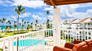 A balcony with a view of a pool, palm trees, and a beach. - Playa Turquesa D-402 Premier Beachfront Ocean View with 50mbps Wifi (Punta Cana)