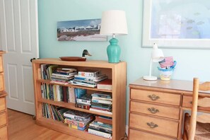 A room with a wooden bookshelf filled with books, a wooden desk with a lamp, and a chair.