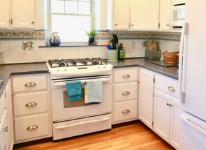 A kitchen with white cabinets, a stove, and a window.