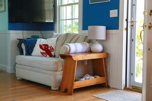 Un salon comprenant un canapé, une table d’appoint en bois, une lampe et un téléviseur fixé au mur.