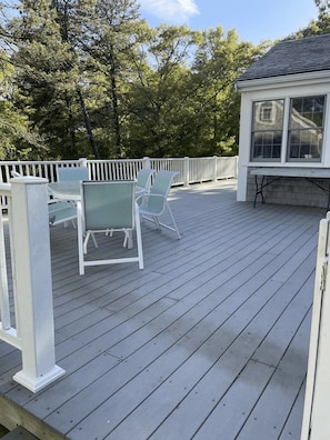 A wooden deck with a white railing, a table with chairs, and a covered area with windows. - Walk To Beach, Hyannisport Three Bedroom! (Barnstable)