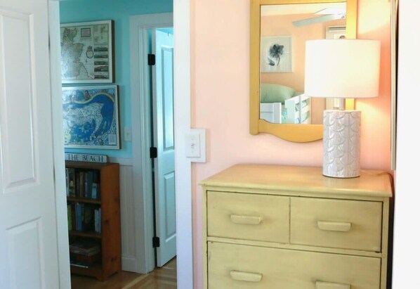 A hallway with a bookshelf, a mirror, and a lamp on a dresser.