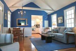 A living room with a blue wall, a chandelier, a sofa, a coffee table, and a dining area with a table and chairs.