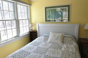 Une chambre à coucher avec un lit, une fenêtre, un radiateur et un tableau encadré accroché au mur.