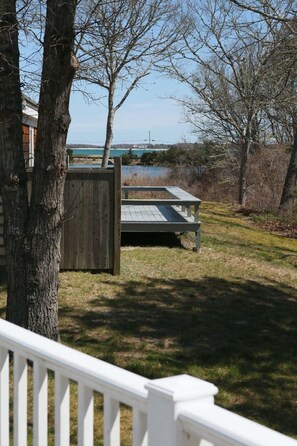A wooden deck with a picnic table, surrounded by trees and a view of a body of water. - Walk To Beach, Hyannisport Three Bedroom! (Barnstable)