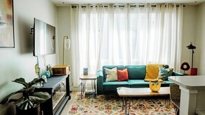 Ein Wohnzimmer mit einem türkisfarbenen Sofa, einem Couchtisch, einem Fernseher und einem gemusterten Teppich.