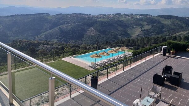 A rooftop pool with lounge chairs and umbrellas, surrounded by a scenic mountainous landscape.