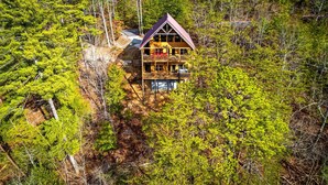 Eine zweistöckige Blockhütte mit einem Balkon, umgeben von dichtem Wald.