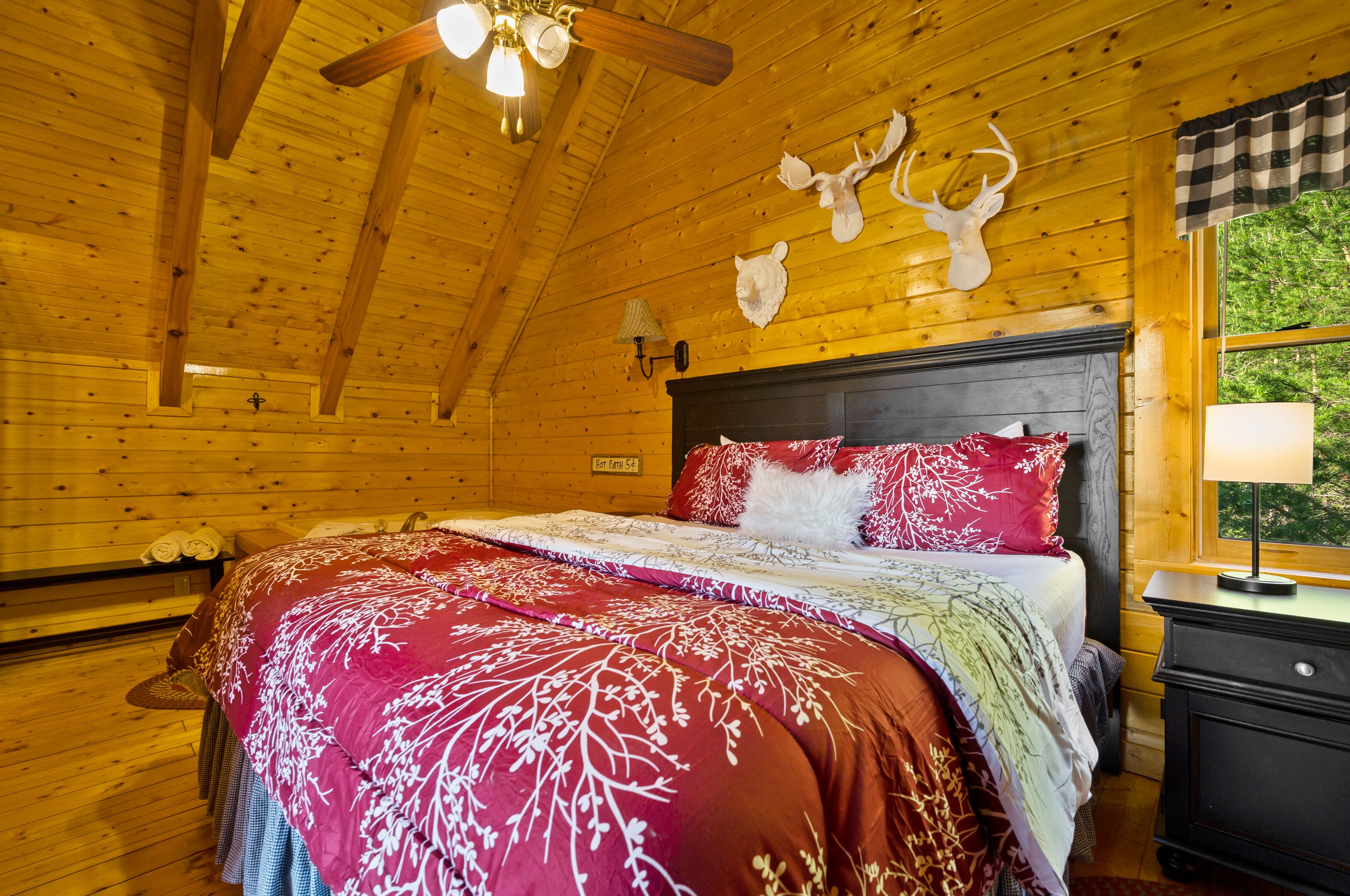 Une chambre dans une cabane en bois, avec un lit, un ventilateur de plafond et des bois de cerf fixés au mur.