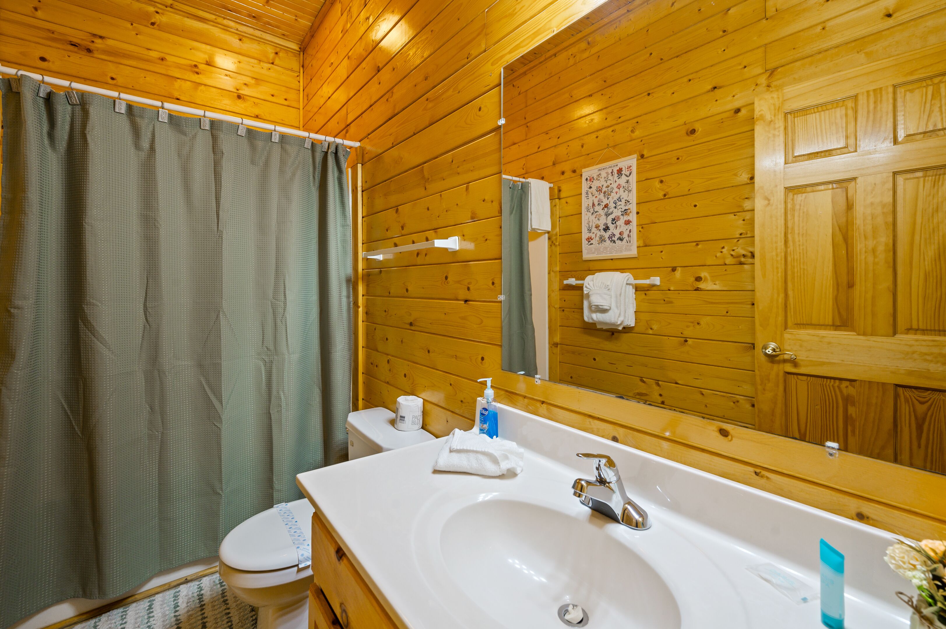 A wooden-paneled bathroom with a white sink, a toilet, and a shower curtain.