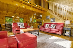 L’intérieur d’une cabane en rondins, avec un escalier, des meubles en cuir rouge et des murs en bois.