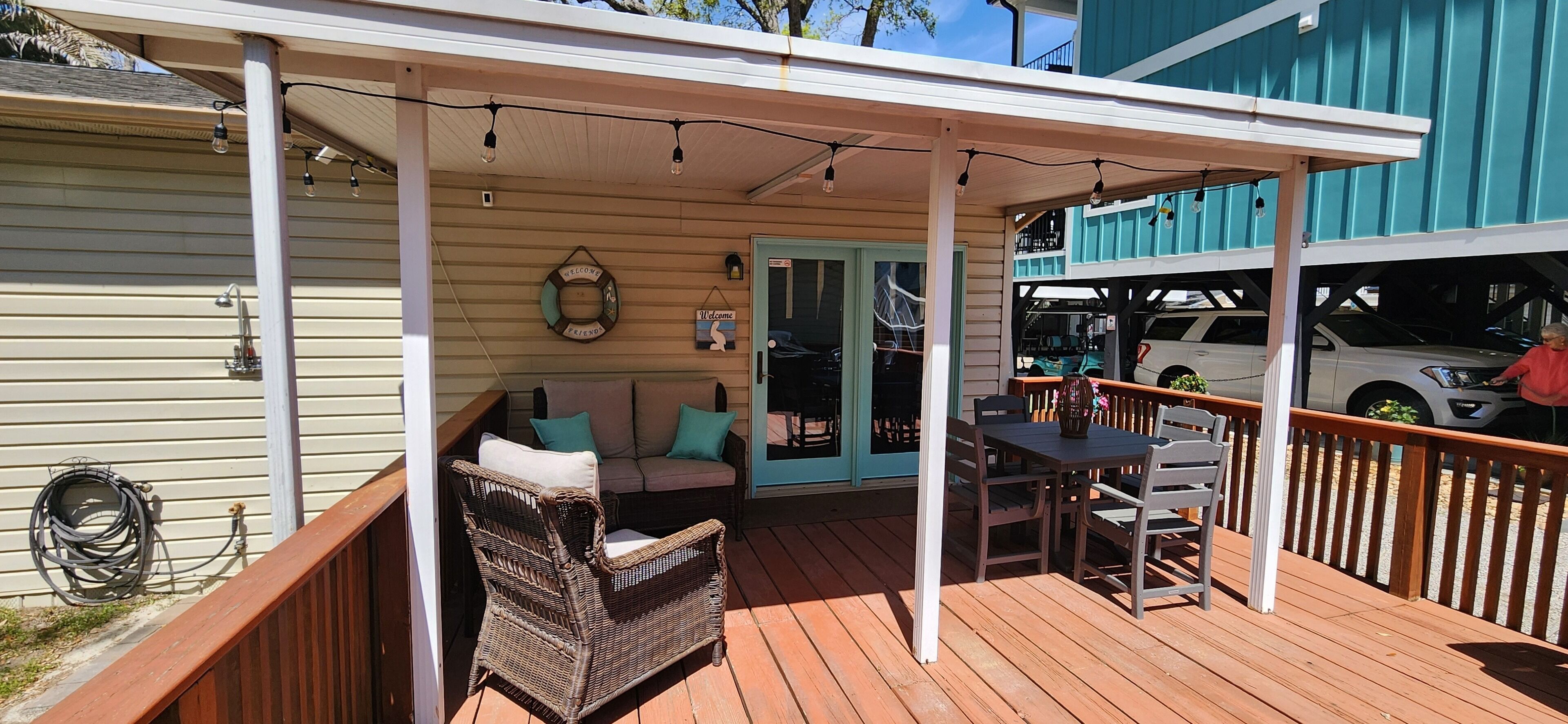 A covered outdoor deck with a sofa and table, a welcome sign, and a vehicle parked nearby.