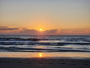 Experience the serene tranquility of a natural beach at sunset, where gentle waves lap at the shore.