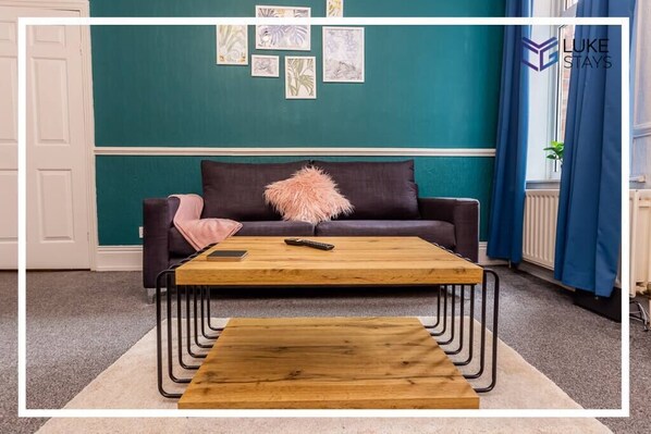 Une pièce aux murs de couleur turquoise, avec un canapé foncé, une table basse en bois et un coussin rose.