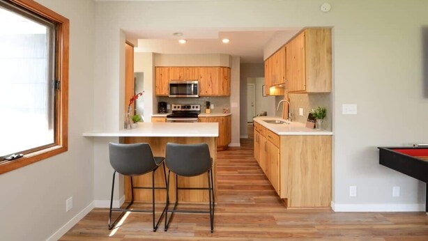 Une cuisine moderne avec des meubles en bois, un îlot central doté de tabourets de bar et une table de billard.