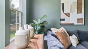 Una habitación con una mesa de madera, un sofá con cojines, una planta grande y un cuadro abstracto colgado en la pared.