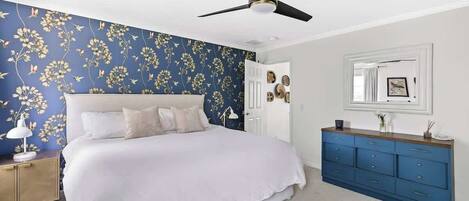 A bedroom with a bed, a ceiling fan, a dresser, and a wall with floral wallpaper.