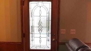 A wooden door with a decorative glass panel, a dark-colored bench, and a light-colored wall with a switch. - Cozy, peaceful "camp" in Hollywood Hills, just north of the town of Old Forge (Old Forge)