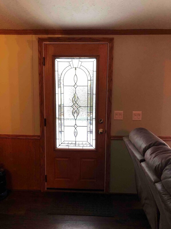 A wooden door with a decorative glass panel, a dark-colored bench, and a light-colored wall with a switch.