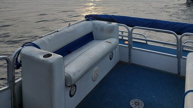 A boat's interior with a blue deck, a white cushioned bench, and a view of the calm water and distant mountains. - Cozy, peaceful "camp" in Hollywood Hills, just north of the town of Old Forge (Old Forge)