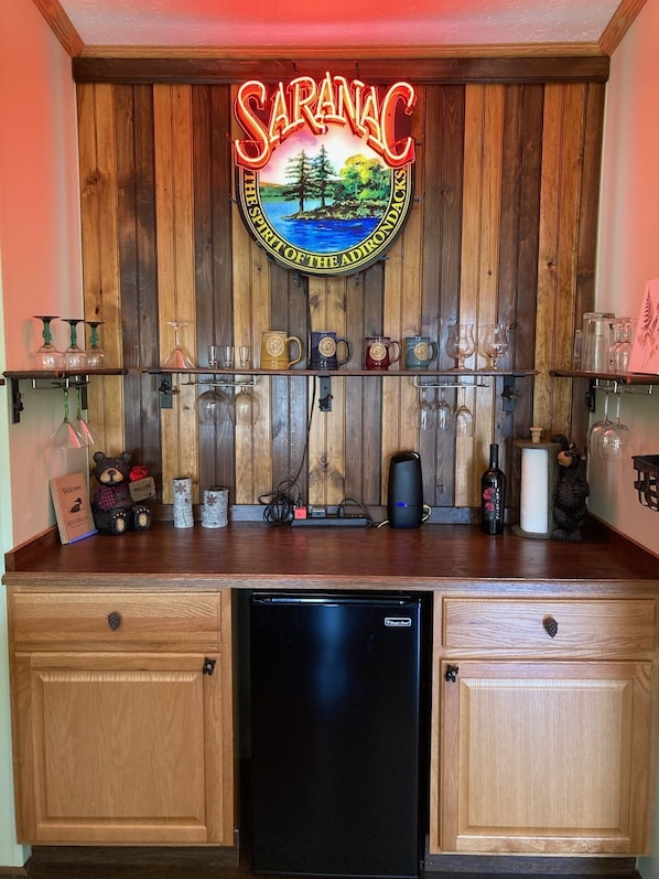 Un comptoir de cuisine orné d’un panneau néon sur lequel on peut lire « Saranac, l’esprit des Adirondacks », un réfrigérateur et divers ustensiles de cuisine.