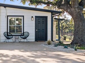 A single-story building with a dark door, two chairs, and a small table outside. - 10 Bedroom / Pool / Hot tub / Pickleball / Firepit (Dripping Springs)