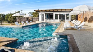 A swimming pool with lounge chairs and a building with a covered patio area. - 10 Bedroom / Pool / Hot tub / Pickleball / Firepit (Dripping Springs)