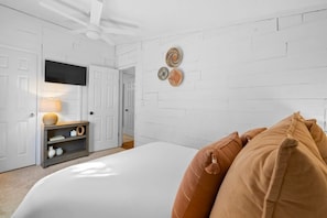A bedroom with a bed, a TV mounted on the wall, a shelf with decorative items, and a door leading to another room. - 10 Bedroom / Pool / Hot tub / Pickleball / Firepit (Dripping Springs)