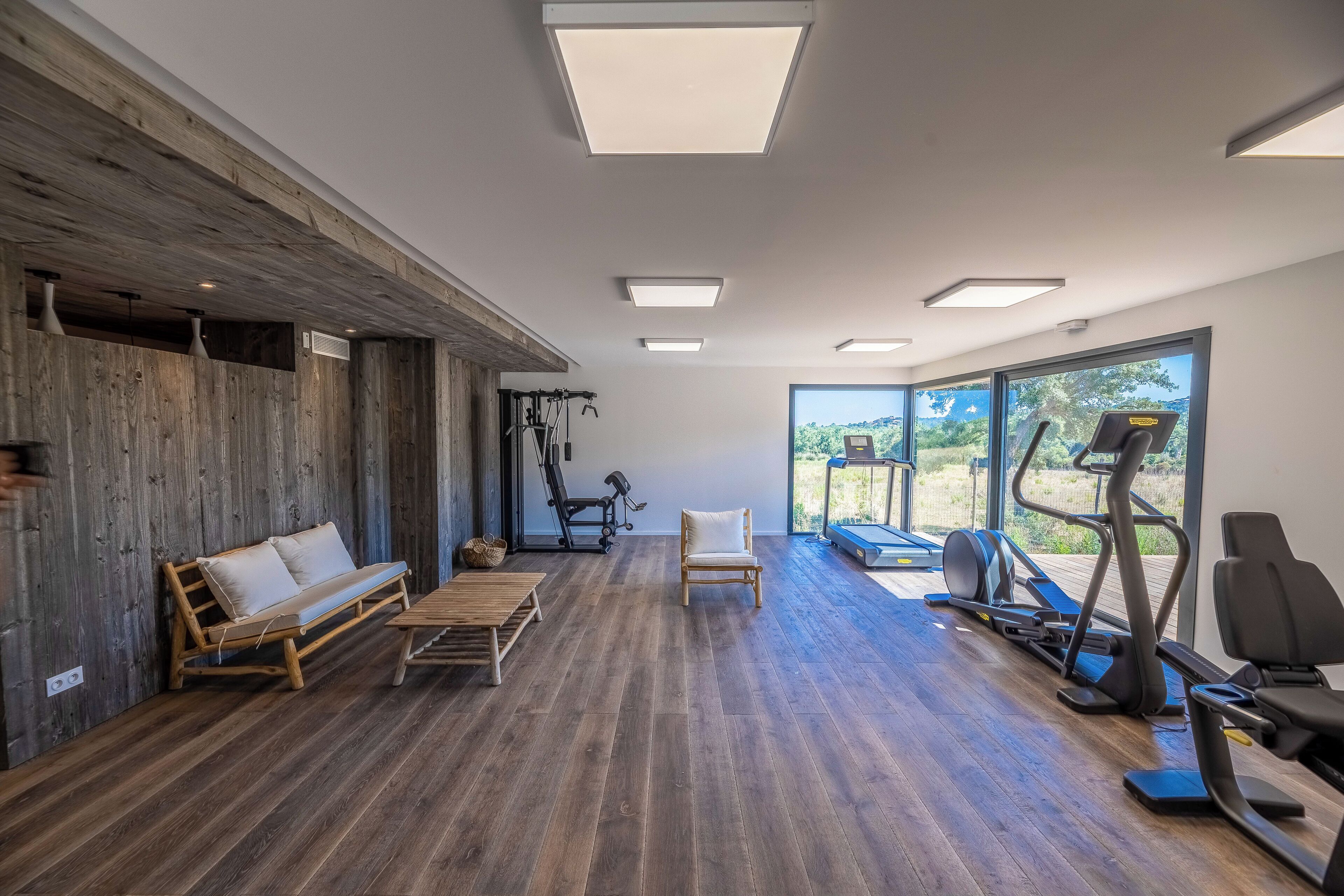 Ein geräumiges Zimmer mit Holzboden, einer Bank, einem Stuhl und Trainingsgeräten.