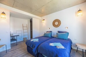 Une chambre avec deux lits, une échelle en bois, une petite table et un luminaire fixé au mur.