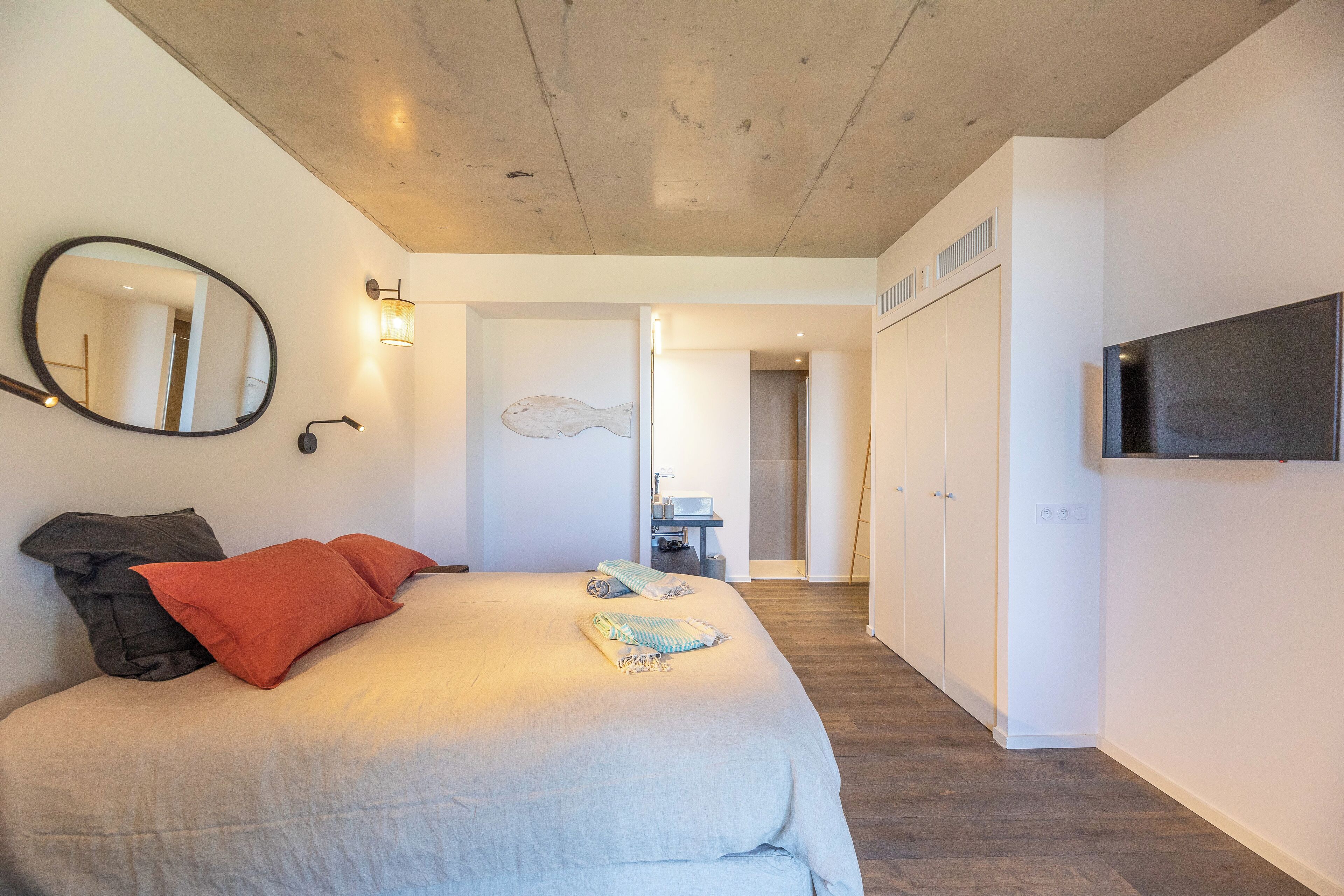 Une chambre à coucher comprenant un lit, un miroir, une télévision et un couloir menant à une salle de bain.
