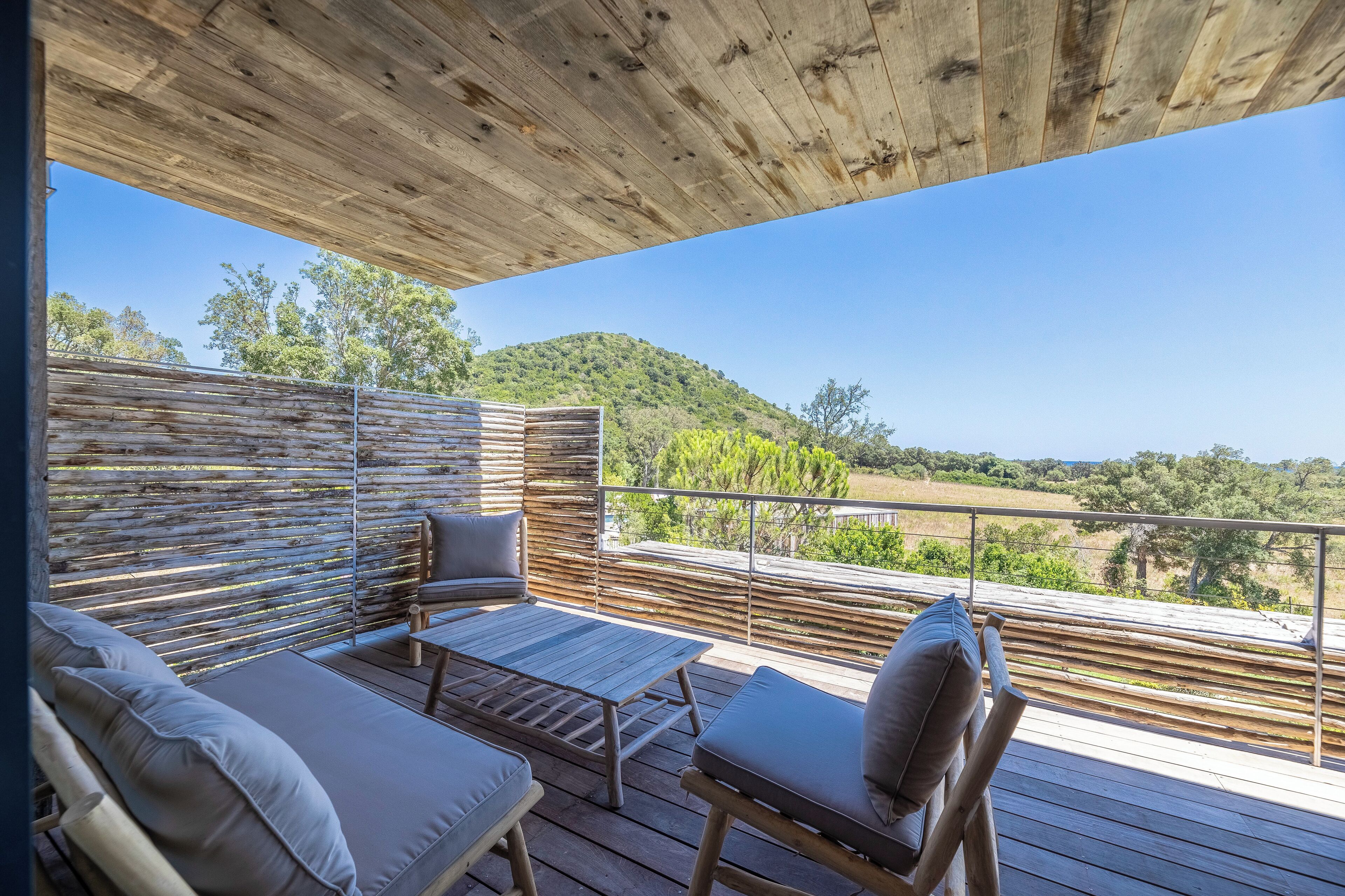Une terrasse en bois avec des sièges d’extérieur, une vue sur un paysage vallonné et un plafond en bois.