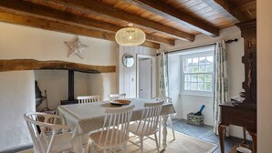 Un espace repas doté d’un plafond en bois, de chaises blanches, d’une table ronde et d’un luminaire suspendu.