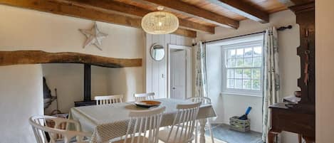 A dining area with a wooden ceiling, white chairs, a round table, and a hanging light fixture.