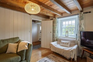 A cozy room with a green sofa, a bed with white bedding, a TV, and a window with curtains.