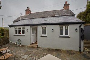 A small, single-story house with a grey exterior, a tiled roof, and a front door.