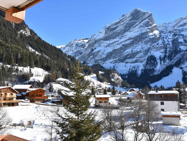 A snow-covered mountain village with wooden houses and a prominent mountain peak in the background.