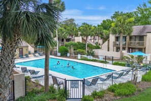 A swimming pool with lounge chairs and palm trees, surrounded by a fence.