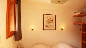 A bedroom with a bed, a small wooden nightstand, a framed picture on the wall, and a shelf with folded towels. - Ski-in/ski-out apartment with indoor pool, close to amenities (Les Orres)