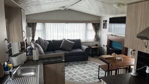 Interior d'una caravana domèstica amb cuineta, sofà, taula de menjador i xemeneia.