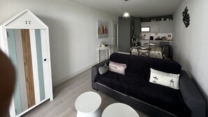 En kompakt opholdsstue med en mørk sofa, et lille hvidt bord og et hvidt skab med en stribet dør.