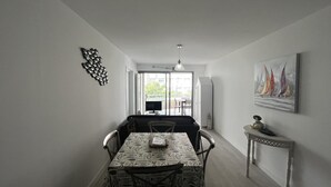 Et spiseområde med et bord dækket til to personer, en sofa og et fjernsyn i baggrunden.