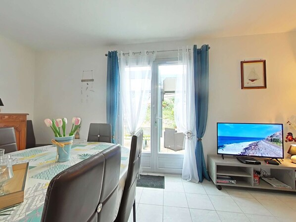 Ein Zimmer mit Esstisch, Stühlen, Fernseher und Blick ins Freie.