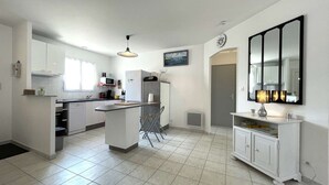 Una cocina moderna con armarios blancos, una isla central y un comedor con mesa y sillas blancas.